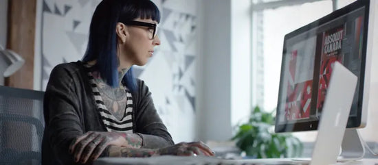 Person with tattoos working on a computer in an office setting