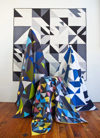 Geometric patterned quilts on a wooden floor with a white wall background