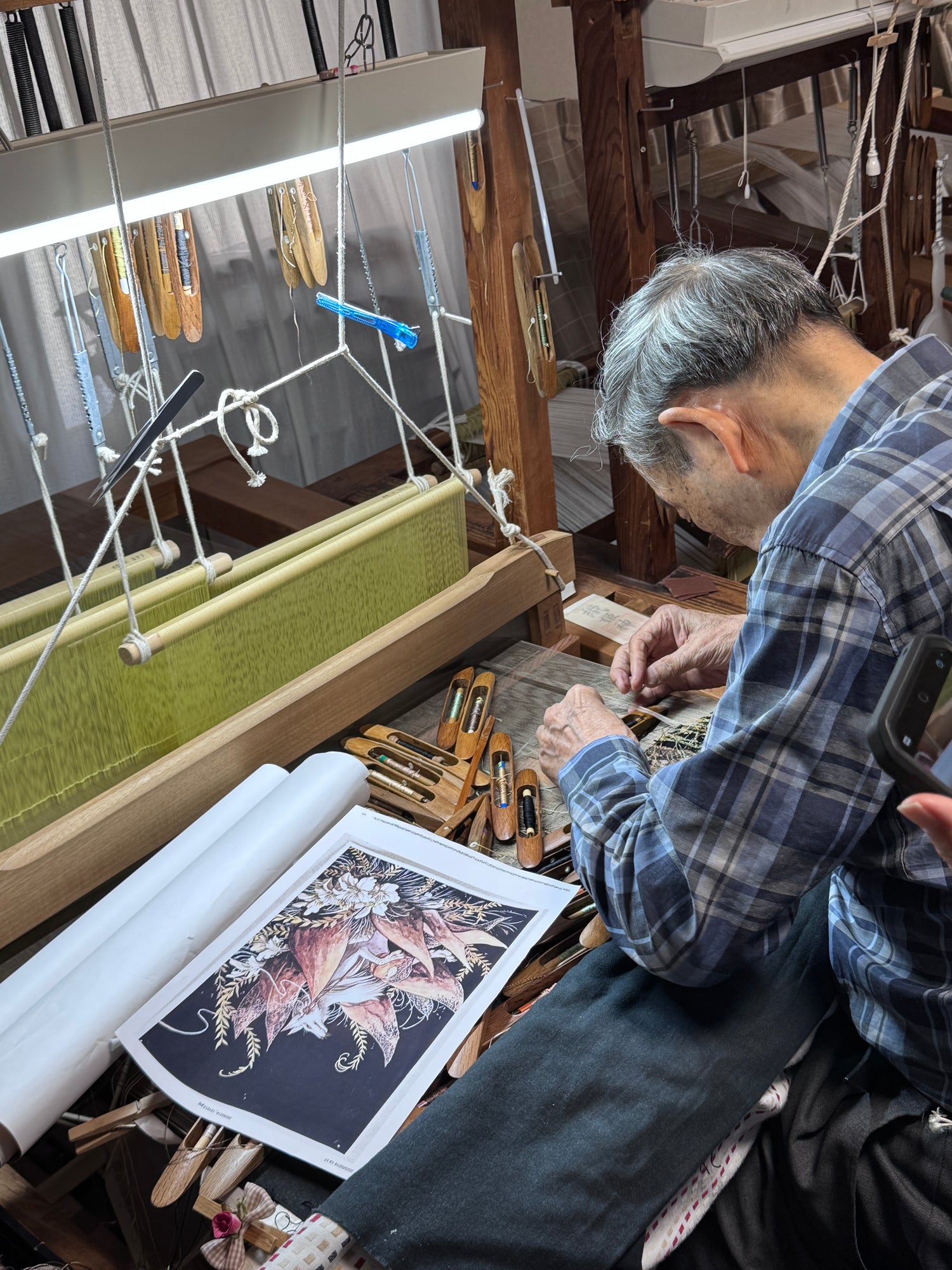 Person working on a weaving loom with various tools and materials around.