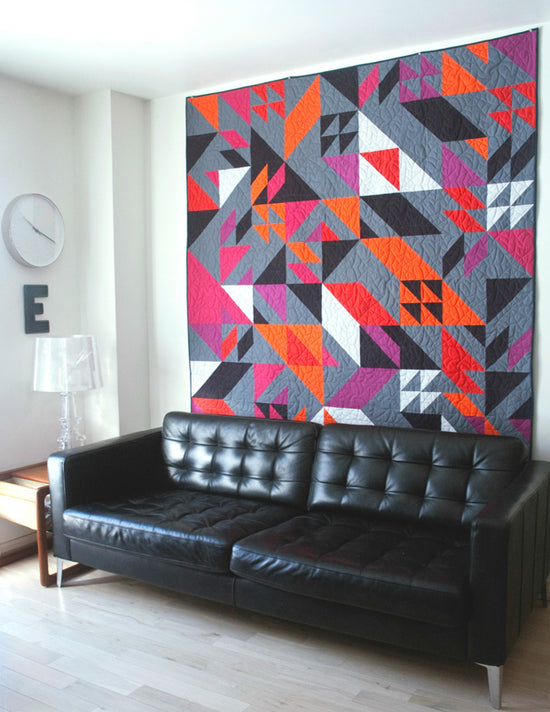 Modern living room with a black leather sofa and a colorful geometric quilt on the wall.