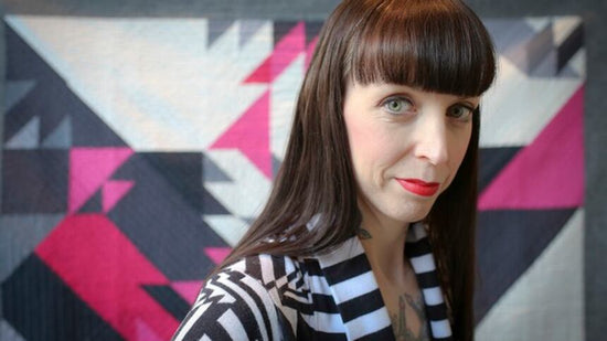 Woman with a striped shirt in front of a colorful geometric-patterned wall.