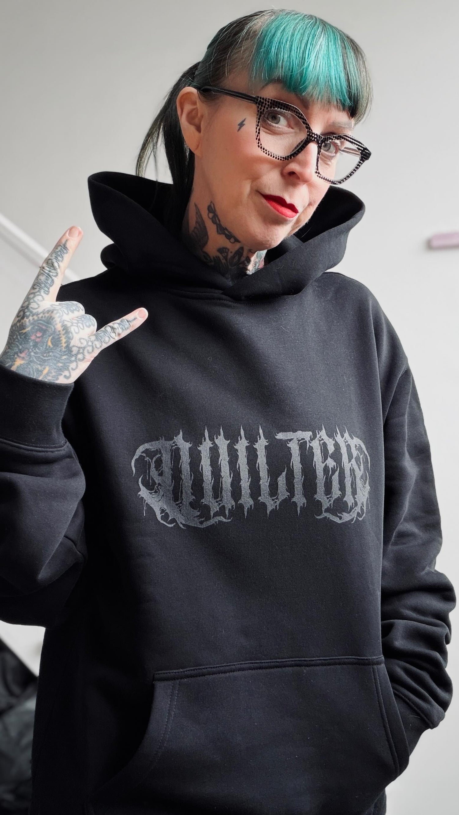 Person wearing a black hoodie with 'Quilted' logo, making a hand gesture.