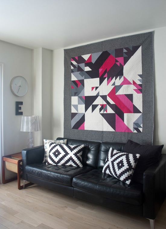 Living room with a black leather sofa, geometric-patterned wall art, and decorative pillows.